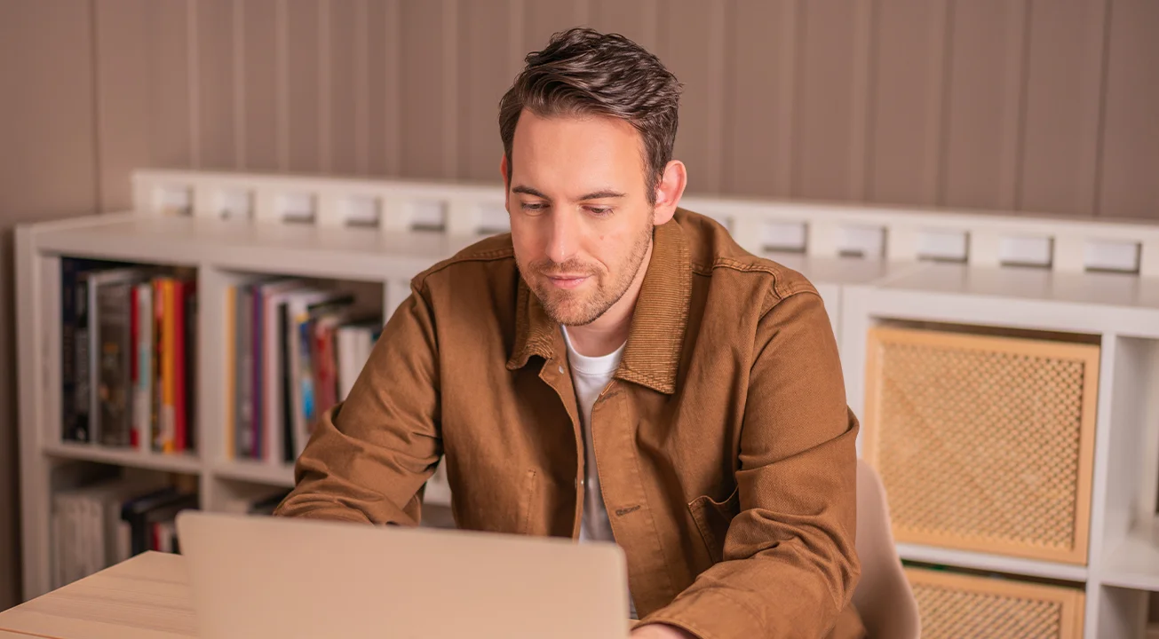Bence Székely, one of the founders of Frem Digital sits at a desk, looking at a laptop. There are books and storage boxes on shelves in the background.