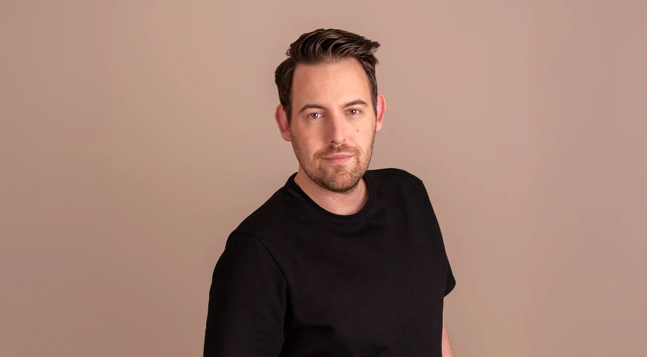 Bence Székely, Co-Founder of Frem Digital, stands against a plain beige background and looks into the camera.