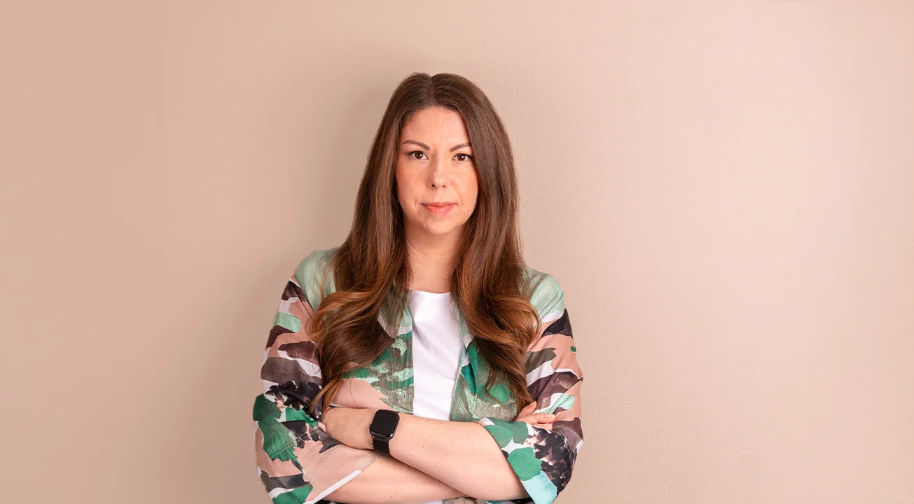Orsi Imreh, the digital advertising expert at Frem Digital, stands against a beige wall. She wears a patterned jacket over a white top, with her arms crossed and a neutral expression.